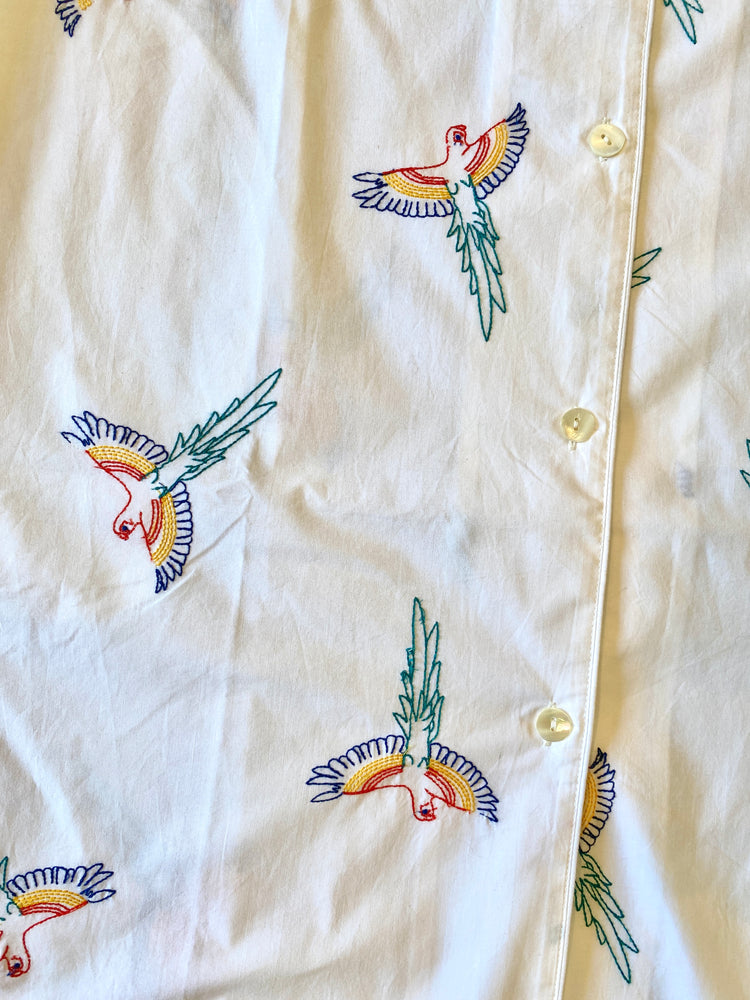 White shirt with colorful bird embroidery on a beige background