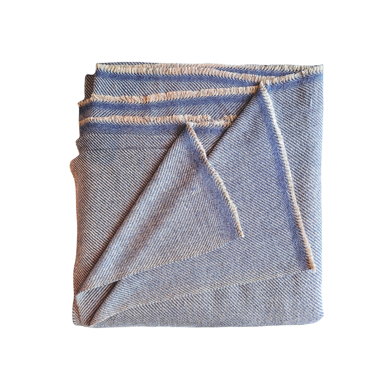 Folded denim fabric on a white background. Muted blue-gray and cream classic herringbone patterned wool throw blanket showing clean lines and fine artisan fringe.