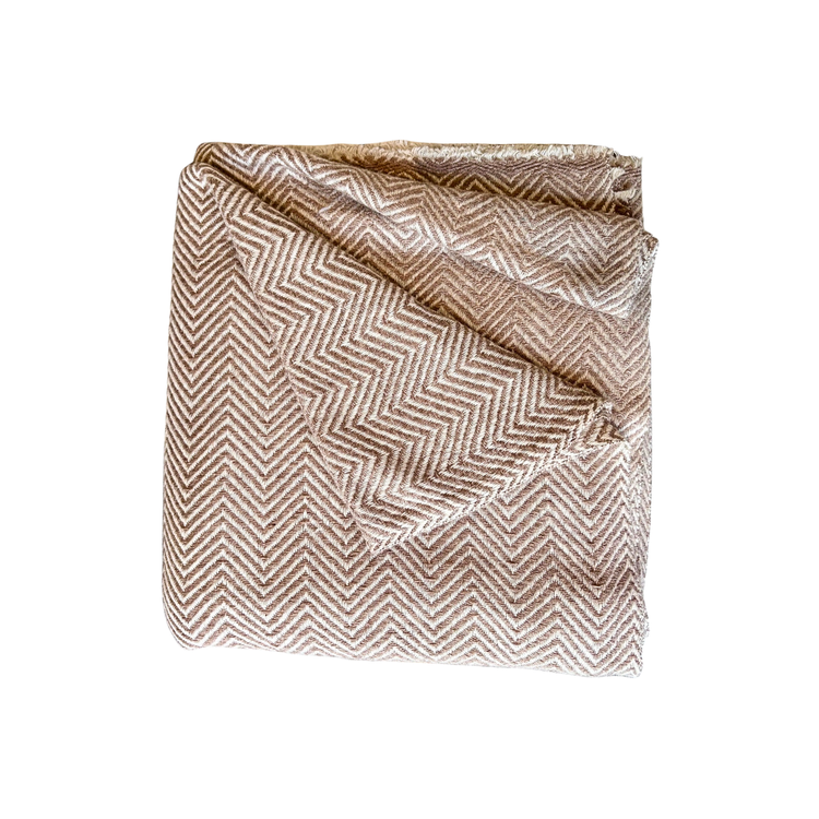 Folded fabric with a herringbone pattern on a white background. Soft tan and cream classic herringbone patterned wool throw blanket with delicate woven fringe details.