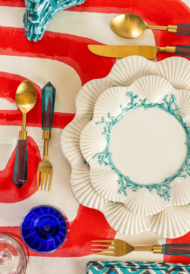 Decorative table setting with gold cutlery, a blue glass, and a red and white striped tablecloth.