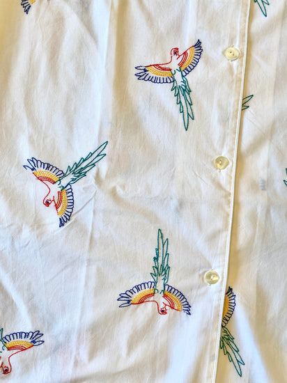White shirt with colorful bird embroidery on a beige background