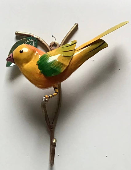 A metal painted hook in the shape of a yellow bird with green and red accents on its wings.