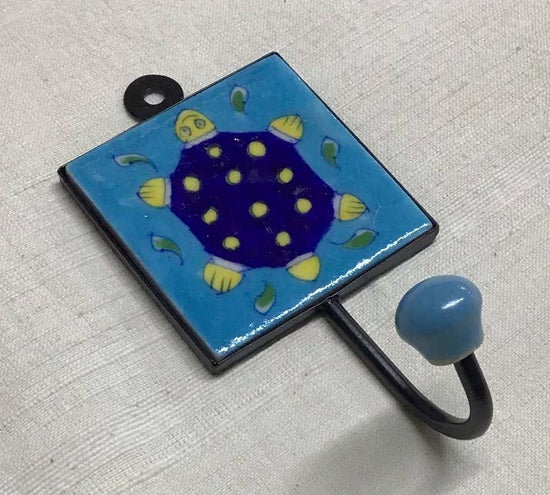 A blue pottery hook with a turtle design, featuring a yellow turtle with dots on a blue background with green leaves.