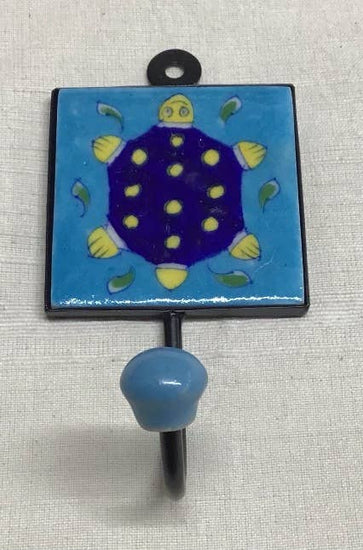 A blue pottery hook with a turtle design, featuring a yellow turtle with dots on a blue background with green leaves.