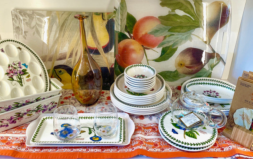 Elegant botanical dinnerware and trays featuring peaches, pears, and toucans, paired with a clear glass teapot and an amber glass vase. A sophisticated, nature-inspired tablescape highlighting biophilic design and artisan treasures.