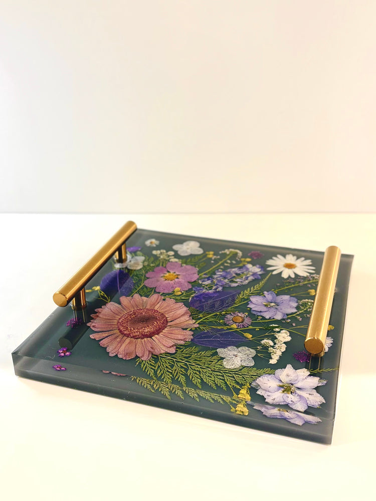 Decorative tray with floral design and gold handles on a white background. Square clear resin tray featuring a beautiful arrangement of embedded dried yellow and red flowers with metallic accent handles.