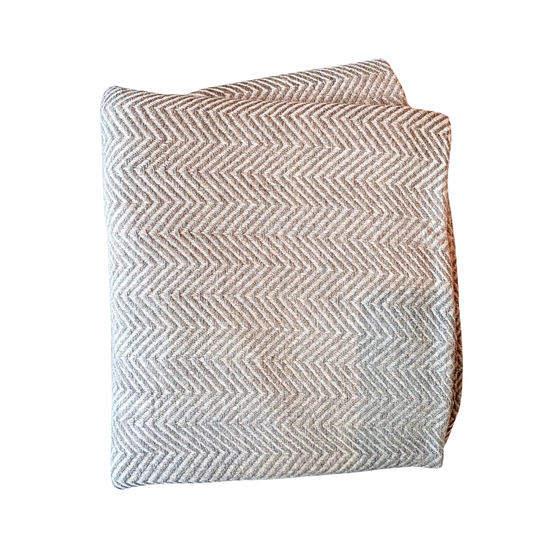 Textured chevron-patterned pillow on a white background. Soft light gray and white herringbone patterned handloomed artisan wool throw blanket displaying refined texture.