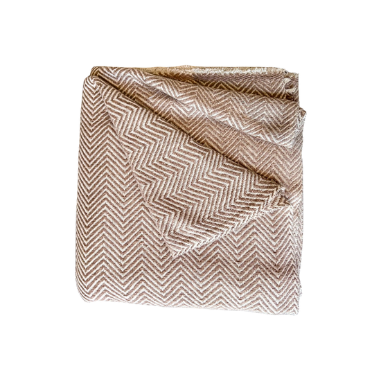 Folded fabric with a herringbone pattern on a white background. Soft tan and cream classic herringbone patterned wool throw blanket with delicate woven fringe details.
