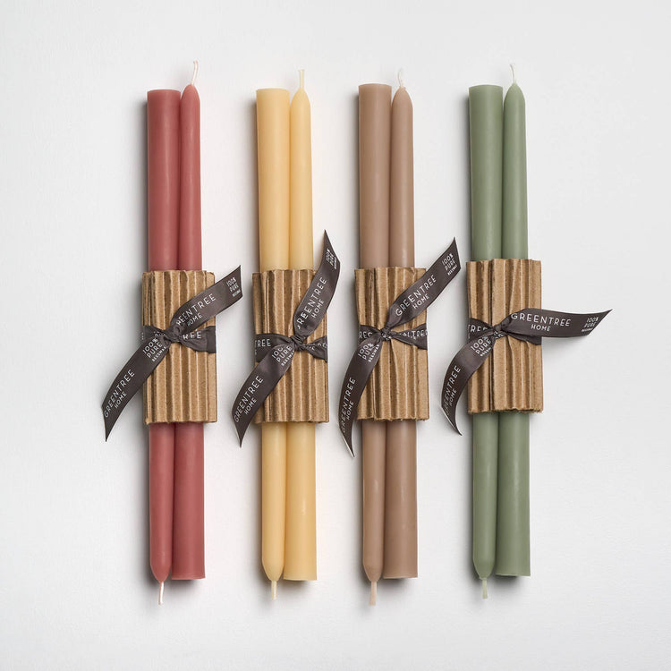 A set of four taper candles in different colors, each with a decorative ribbon around the base, displayed against a white background.