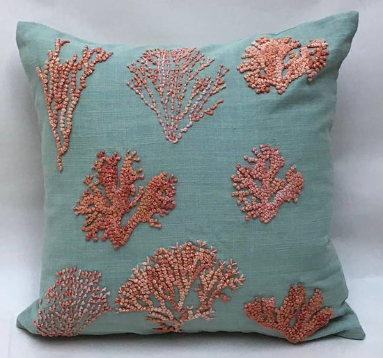 A square-shaped blue pillow with a whimsical embroidered applique of knotty coral in pink and orange hues on teal.